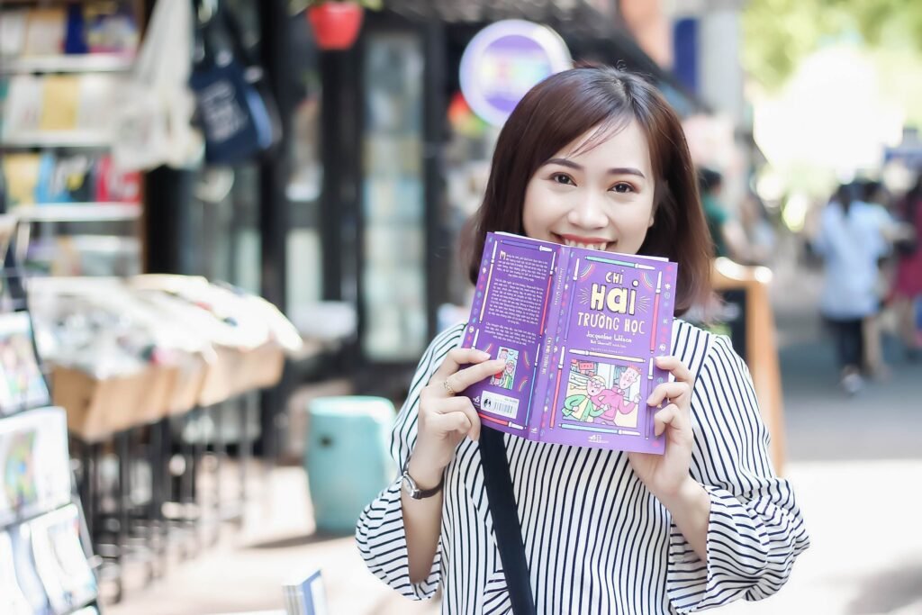 Mengapa Buku Tanpa ISBN Ibarat Pengembara Tanpa Paspor: Nyawa Kedua di Balik Manifestasi Pemikiran Cheerful woman reading a book in a vibrant outdoor setting, enjoying a sunny day in the city.